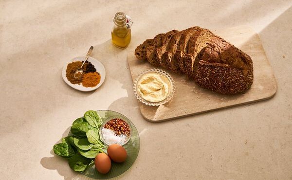 Ingredients for protein-rich vegetarian toast: seeded bread, hummus, spinach, spices, eggs and olive oil.