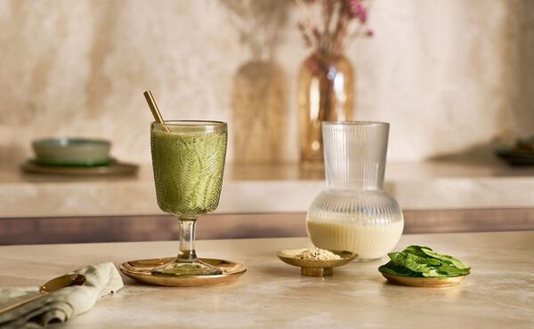 Glass of green protein smoothie with spinach, hemp seeds, and milk on a marble counter.