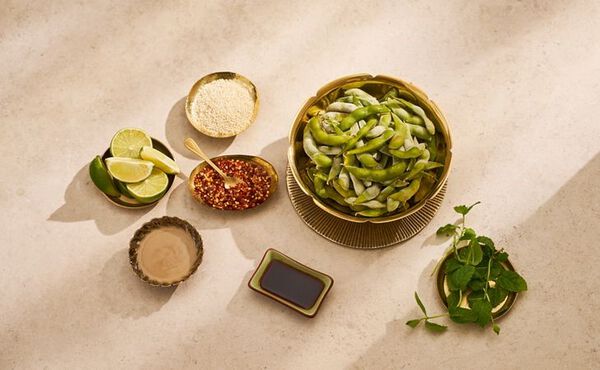 Bowl of edamame beans with lime, chili flakes, sesame seeds, and soy sauce for a healthy protein snack.
