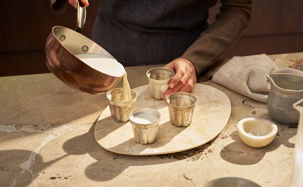 Pouring creamy yuzu panna cotta mixture into metal cups to set, part of an easy dessert recipe.