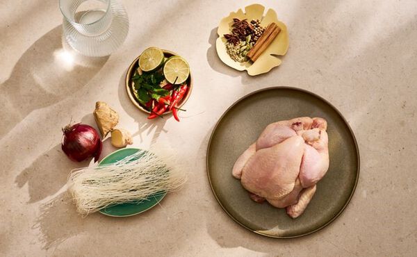Fresh ingredients for homemade chicken pho, including a whole chicken, rice noodles, ginger, lime, chilli and spices.